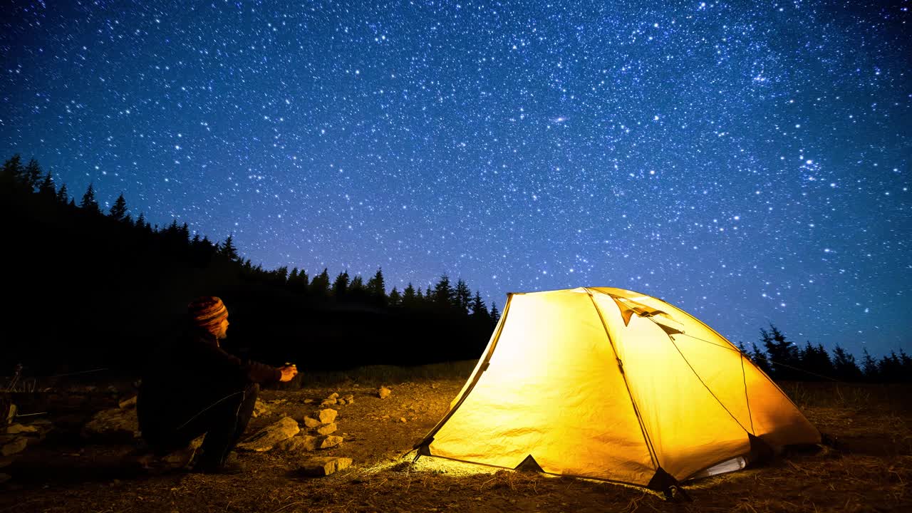 旅行者在闪烁的星空背景下，靠近发光的露营帐篷。Cinemagraph。视频素材