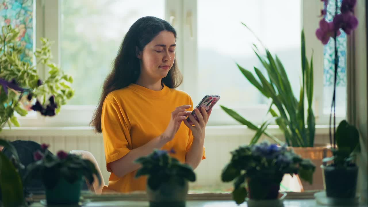 一个很开心的年轻女人坐在窗边用手机视频通话。室内自然植物。真正的时间。互联网通信的概念视频素材