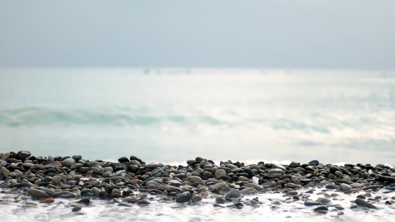 海浪拍打在卵石滩上。镜头的焦点从海岸转移到地平线，那里有一群鸟在游泳。慢动作视频素材