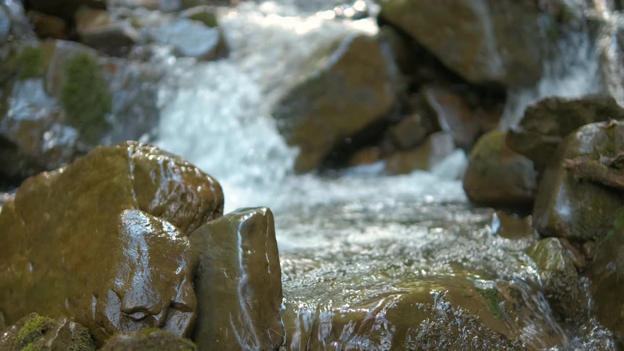 靠近小山涧与清澈的蓝色水流动之间潮湿的石头在夏季森林。视频素材