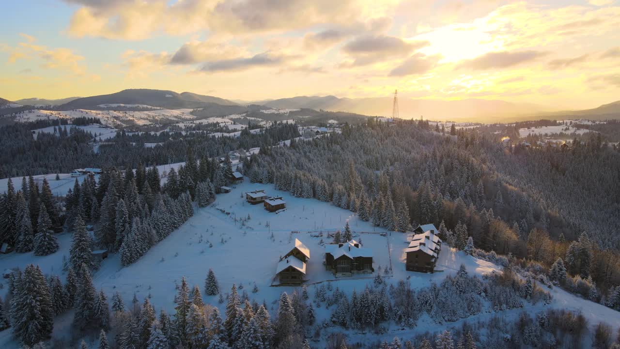 空中冬季景观与小村庄房屋之间的雪覆盖森林在寒冷的山在晚上。视频素材