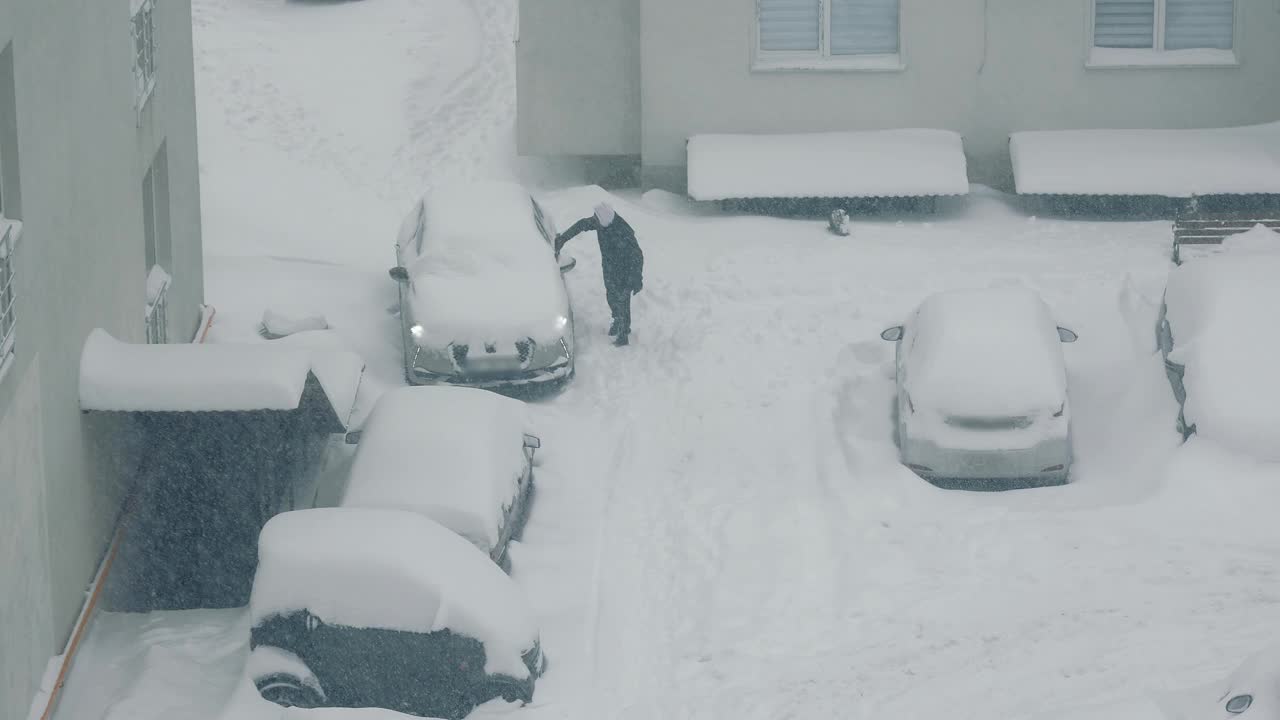 俯视图，一名男子正在清理一辆停在雪旁的汽车。大雪视频素材