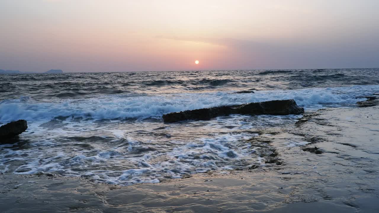 日出时的海岸线景观，太阳在地平线上，海浪拍打着海岸。视频素材