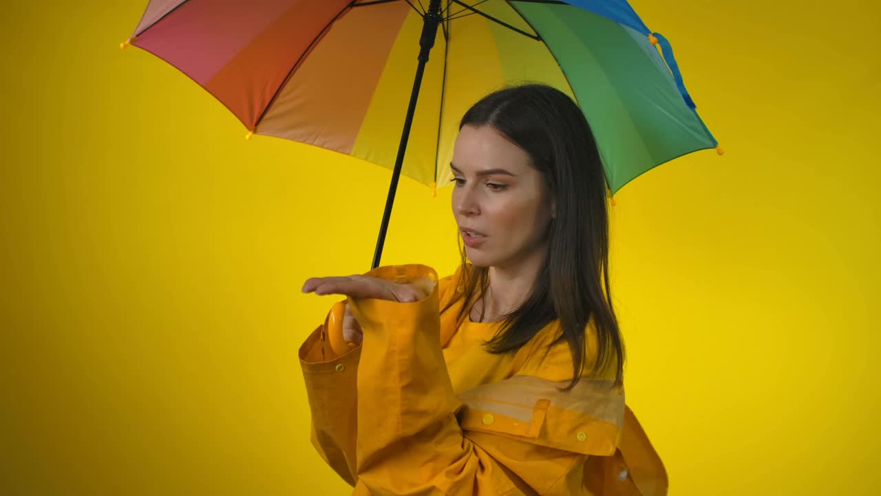 一位身穿黄色雨衣、撑着彩虹伞的妇女正在检查是否下雨视频素材