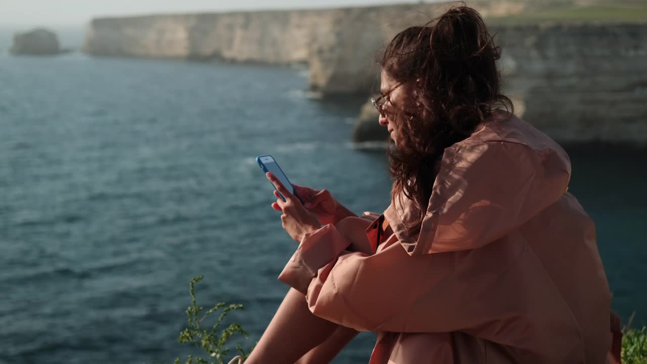 女人坐在海边，用智能手机在线聊天视频素材