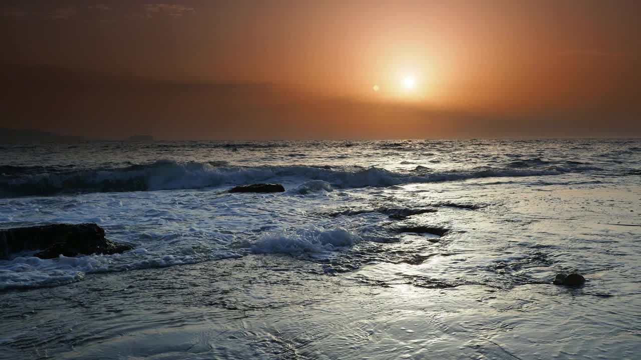 日出时的海岸线景观，太阳在地平线上，海浪拍打着海岸。视频素材