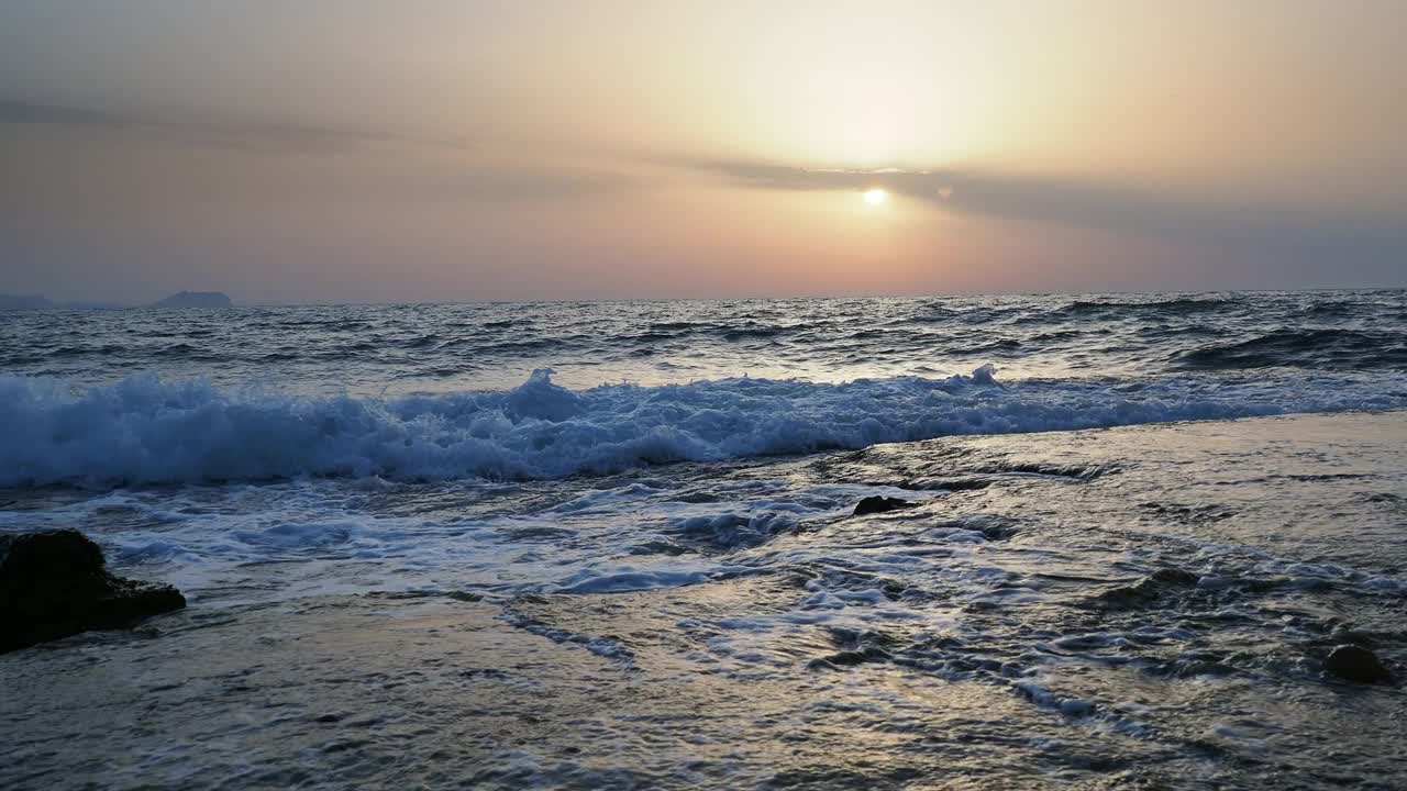 日出时的海岸线景观，太阳在地平线上，海浪拍打着海岸。视频素材