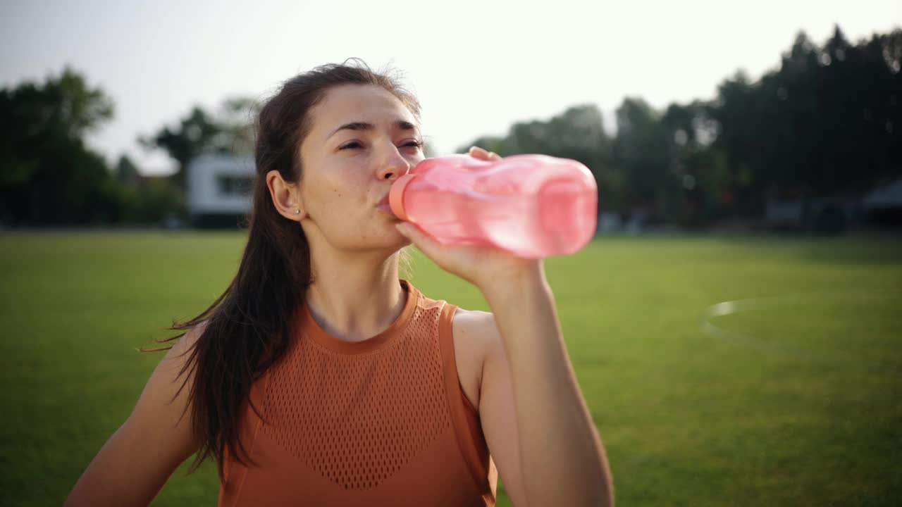 靠近女人在日落喝水，年轻女子运动员在橙色t恤视频素材