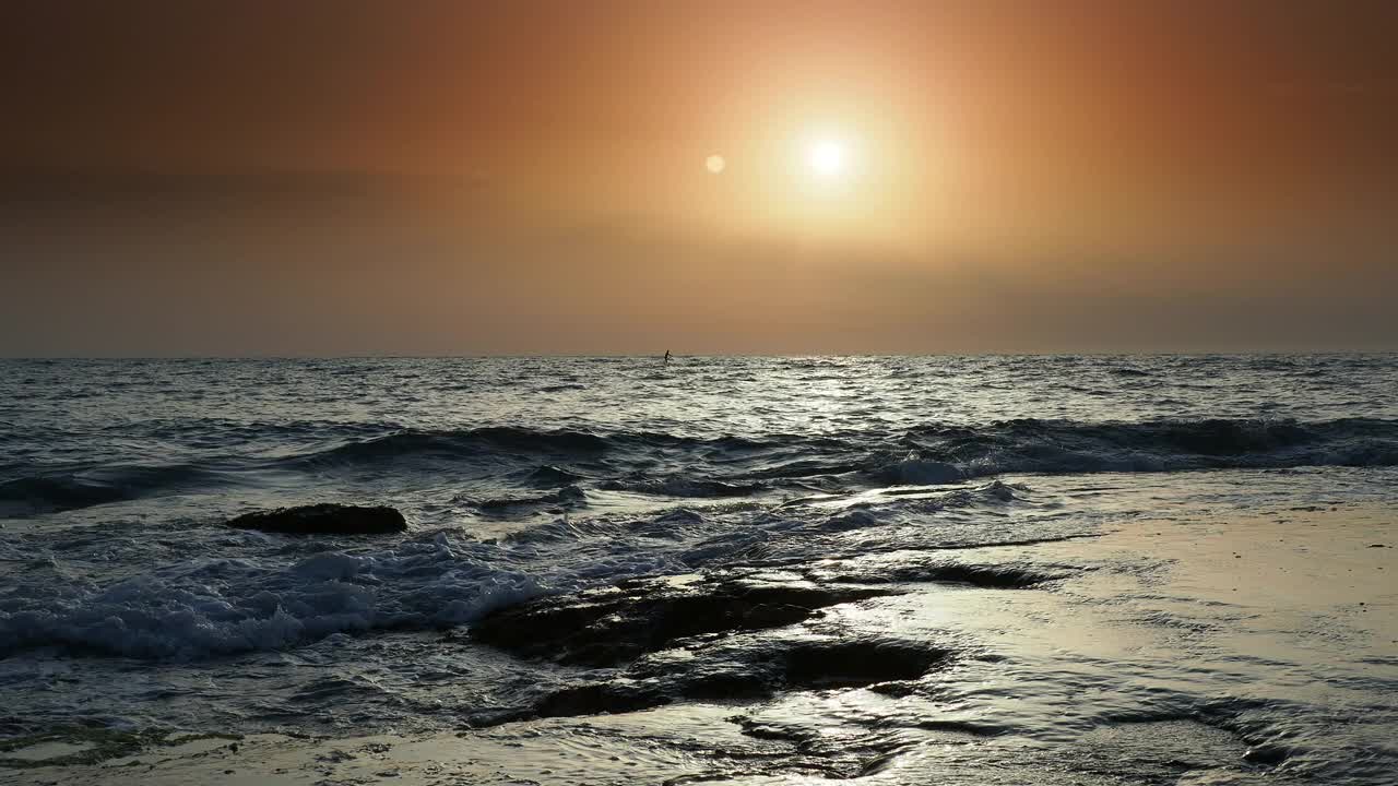 日出时的海岸线景观，太阳在地平线上，海浪拍打着海岸。视频素材