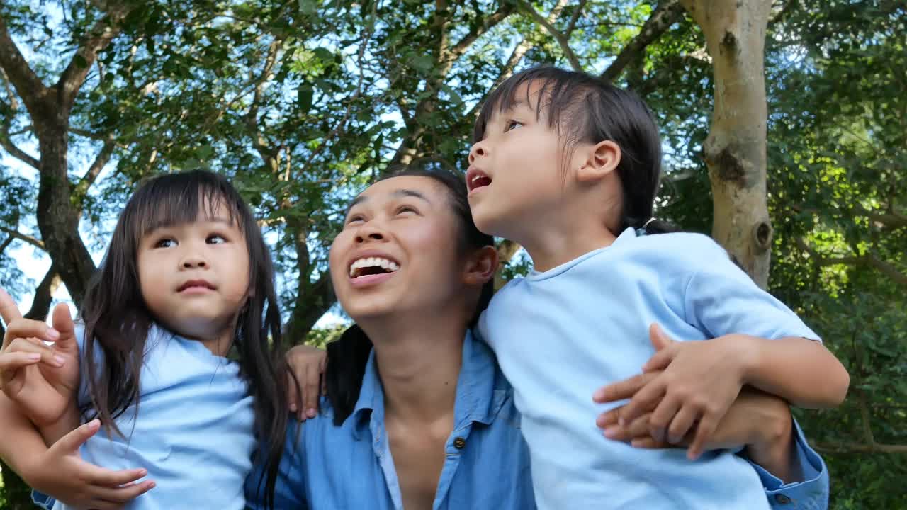 在温暖阳光的夏日，两个兄弟姐妹和妈妈在花园里欢笑和拥抱。小女孩和妈妈在公园里玩。视频素材