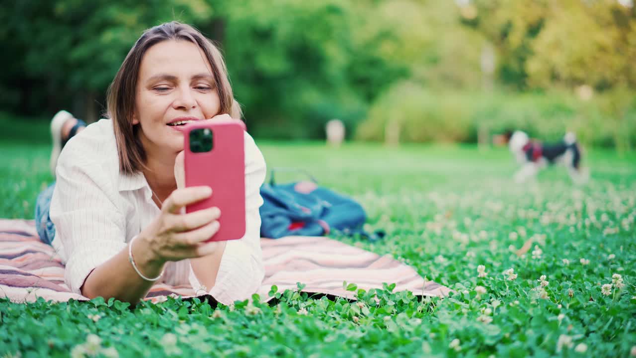 一个漂亮的成年女人在公园里用智能手机拍视频。视频素材