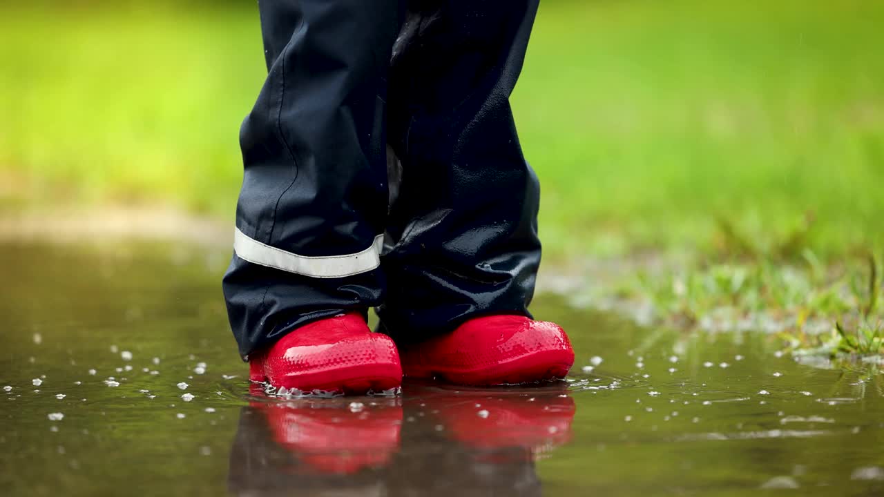 穿着红色胶靴的孩子在雨坑里跳。防水服装视频素材