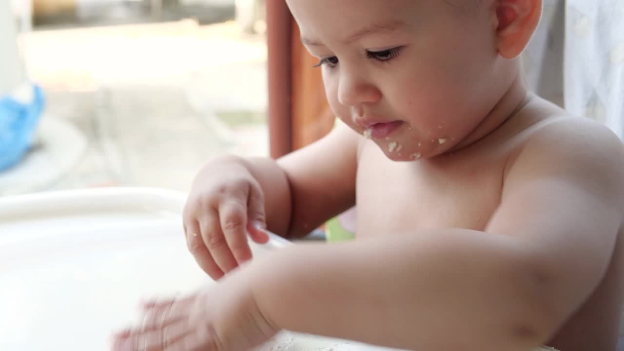 一个用勺子吃婴儿食品的孩子的肖像。母亲在户外孩子的餐桌旁喂孩子视频素材