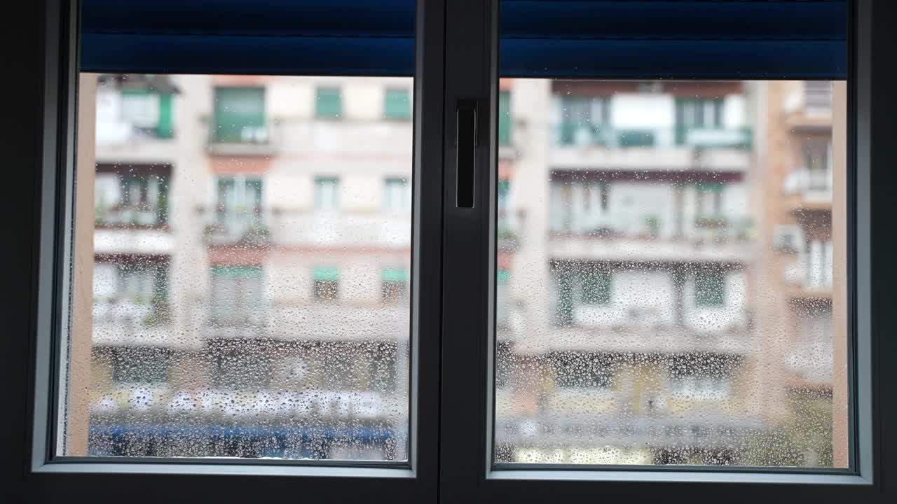 从室内看雷雨后潮湿的窗户表面，雨天模糊的住宅建筑背景上蓝色百叶窗关闭的窗户。心情沉重时悲伤视频素材