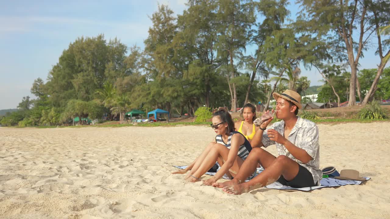 一群亚洲男人和女人朋友在夏天的假期在海滩上野餐视频素材