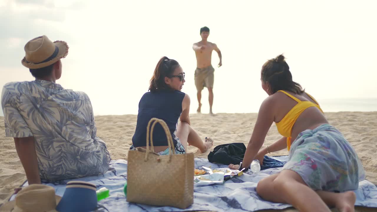 一群亚洲男人和女人朋友在夏天的假期在海滩上野餐视频素材