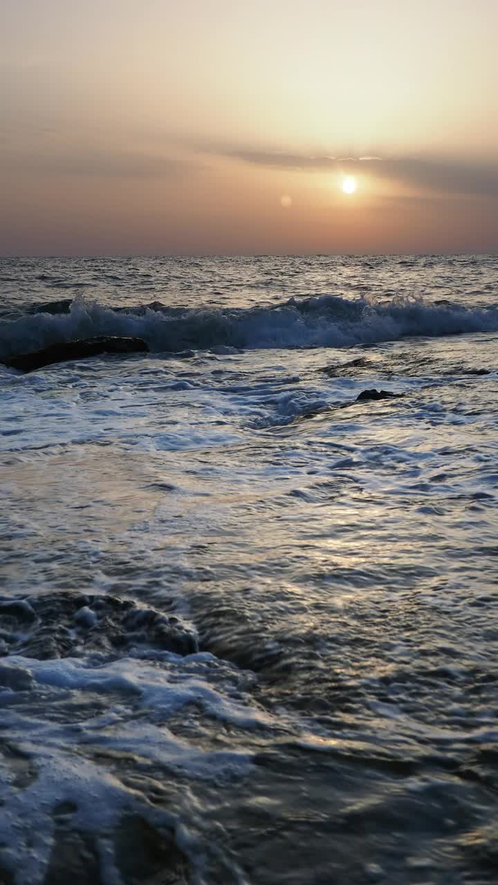 日出时的海岸线景观，太阳在地平线上，海浪拍打着海岸。视频素材