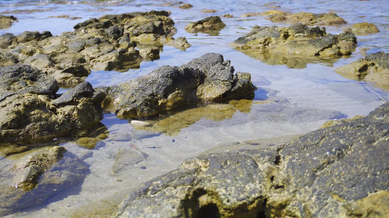 沙滩上浅水中的岩石，海浪拍打着石头视频素材