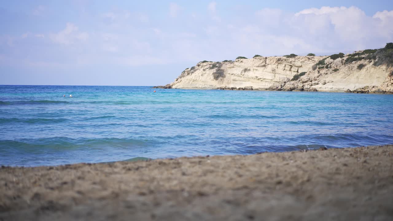 宽阔的镜头清晰的蔚蓝的地中海海浪在沙滩上滚动与岩石在阳光的背景。户外避暑胜地的美丽风景。自然美的概念。视频素材