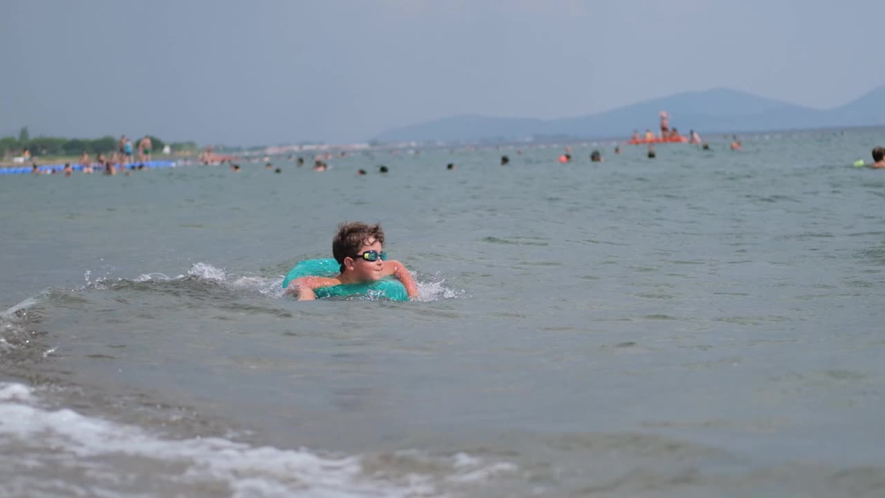 小男孩喜欢拿着橡皮圈在海里游泳。视频素材