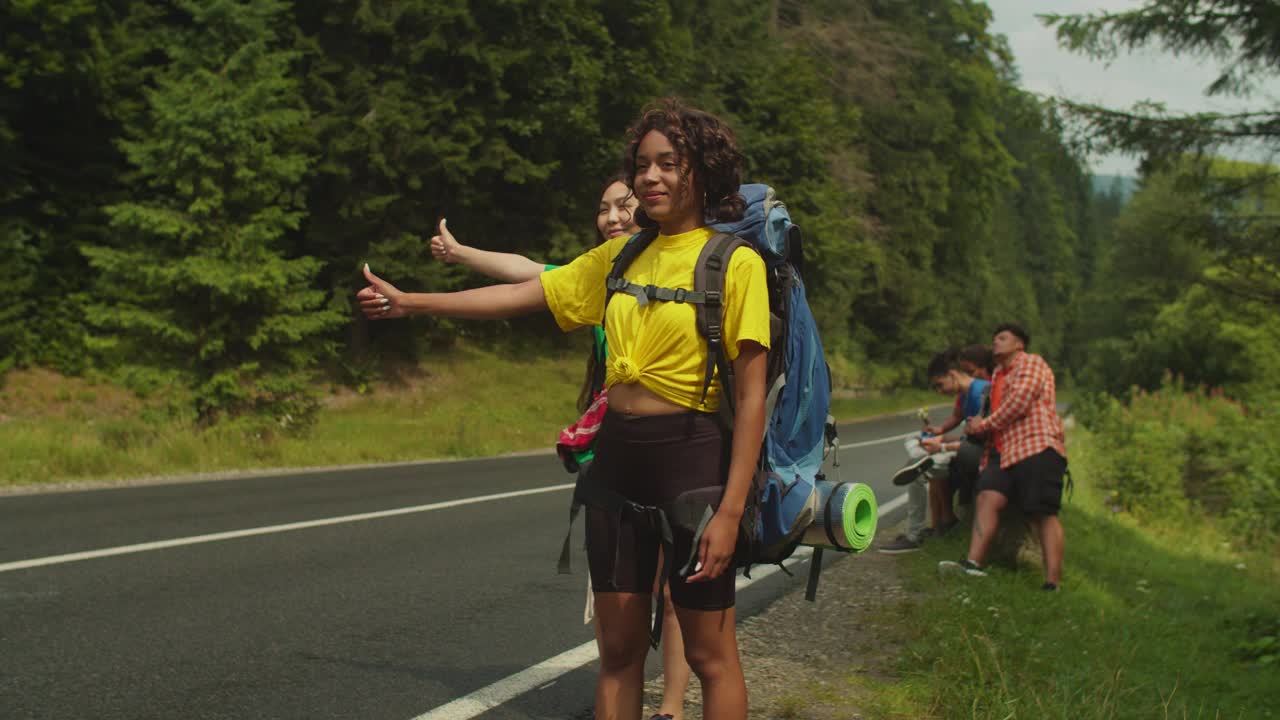 开朗可爱的多民族女性旅行者在山路上搭便车视频素材