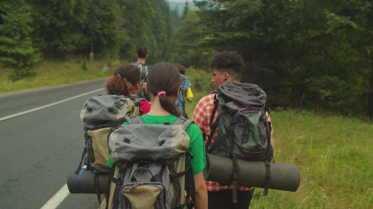 一群活跃的多种族游客背着背包在山区的公路上徒步旅行视频素材