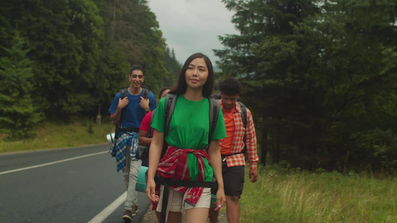 快乐的多元文化游客背着背包沿着高速公路在山上徒步旅行视频素材