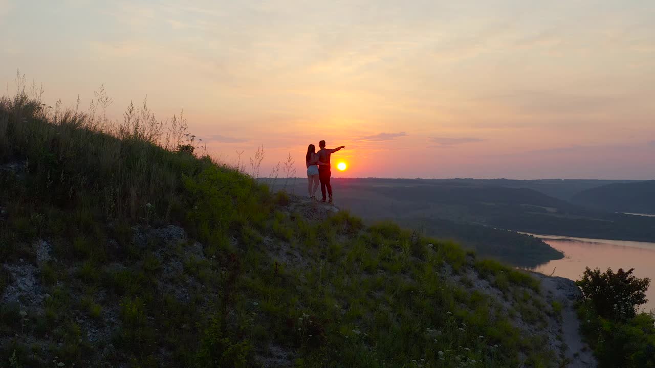 这对浪漫的情侣站在山坡上，看着美丽的夕阳视频素材