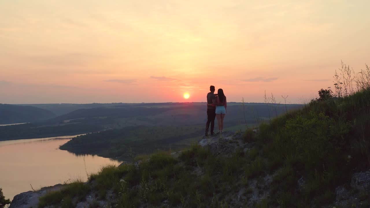 这对浪漫的情侣站在山坡上，看着美丽的夕阳视频素材