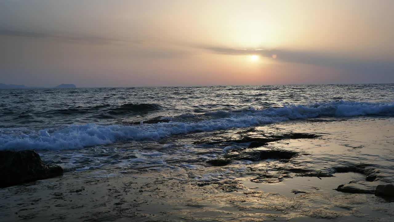 日出时的海岸线景观，太阳在地平线上，海浪拍打着海岸。视频素材