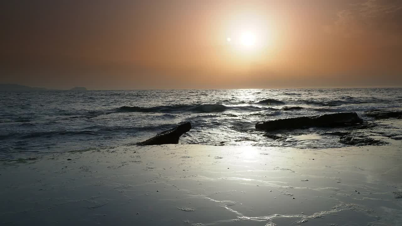 日出时的海岸线景观，太阳在地平线上，海浪拍打着海岸。视频素材