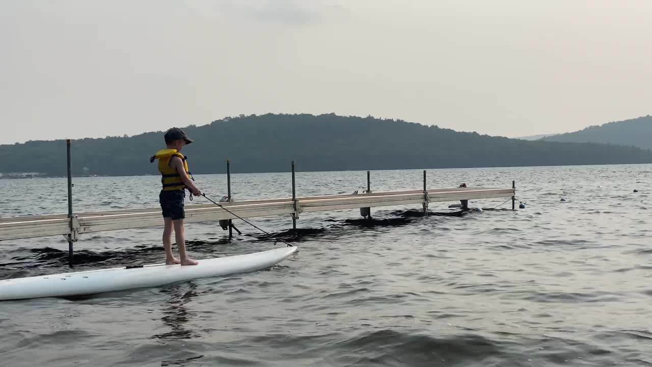 可爱的男孩在夏天的日落湖上冲浪视频素材