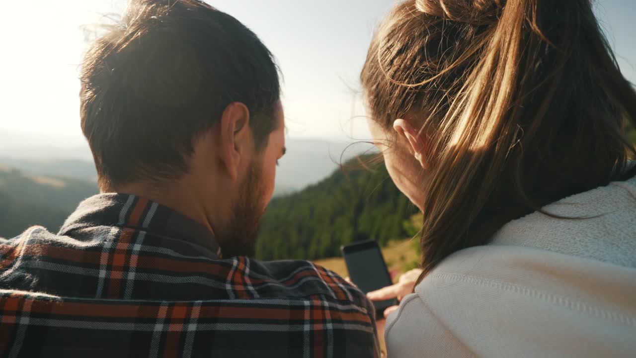 年轻夫妇在山上放松时使用智能手机。视频素材