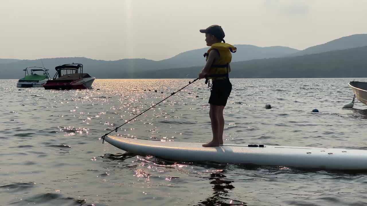 可爱的男孩在夏天的日落湖上冲浪视频素材