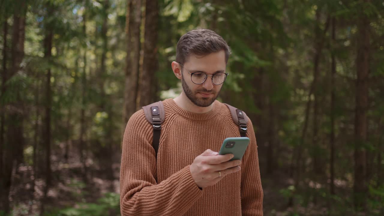 一名男性旅行者背着背包，拿着手机正在穿越森林。GPS，导航仪，在线地图，位置搜索。利用手机上的应用程序对地形进行定位。视频素材