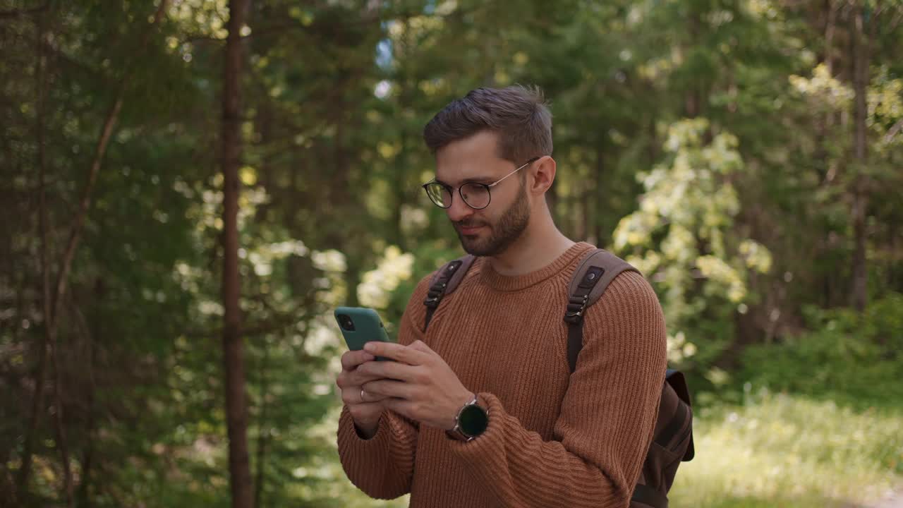 一名背着背包的男性旅行者在森林里的一条土路上行走，写信息，在互联网上交流，查看内容。视频素材