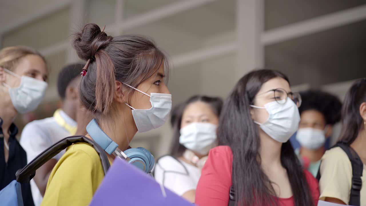 一群戴着防护口罩的青少年学生。回到学校，采取安全措施应对冠状病毒。视频素材