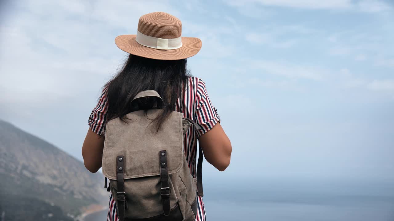 优雅的女游客戴着草帽，从山顶欣赏海景视频素材