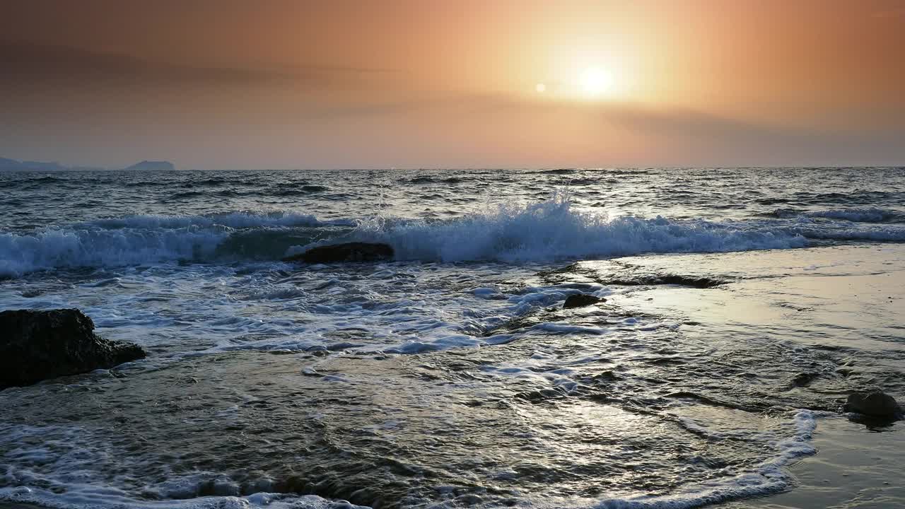 日出时的海岸线景观，太阳在地平线上，海浪拍打着海岸。视频素材