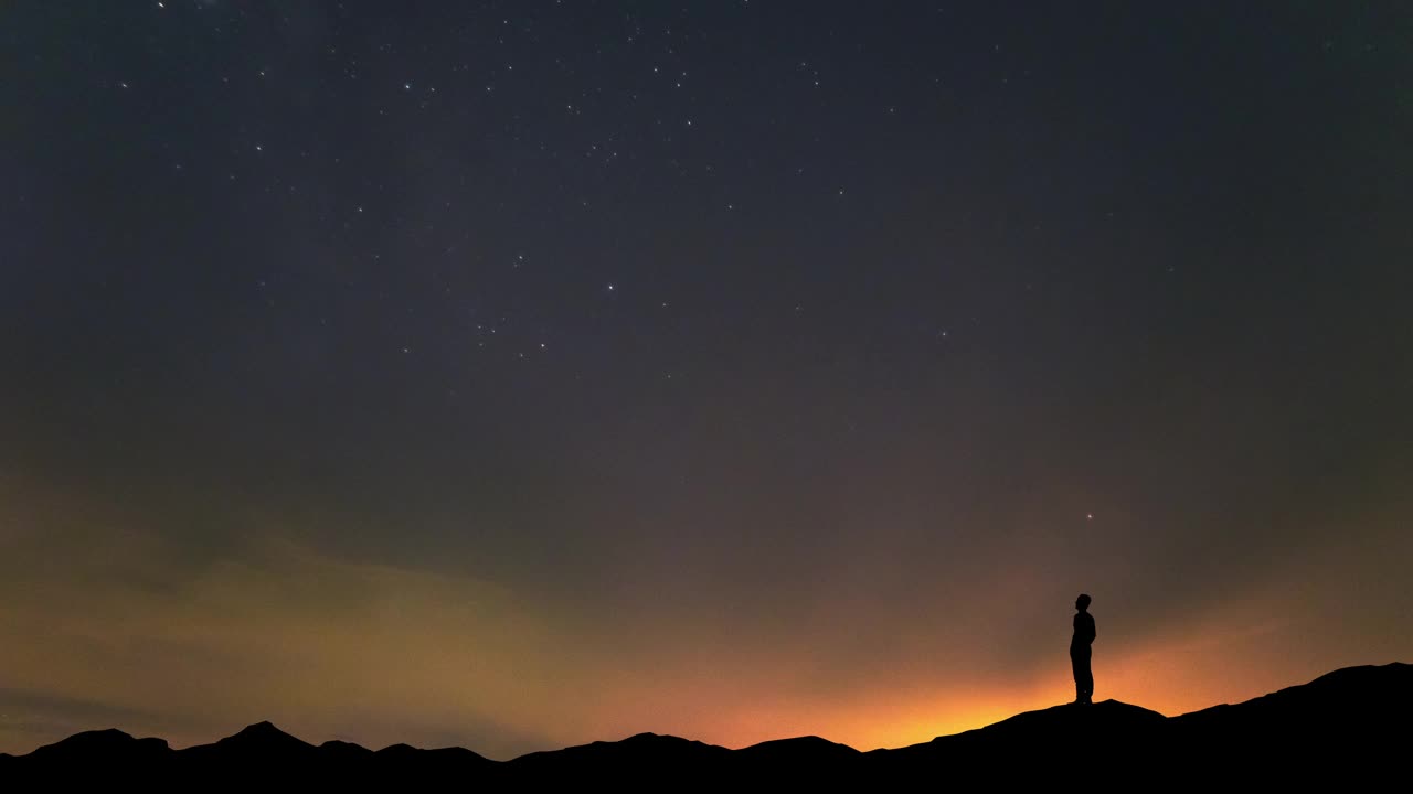 这个人站在山顶上，背景是美丽的夜空。时间流逝视频素材