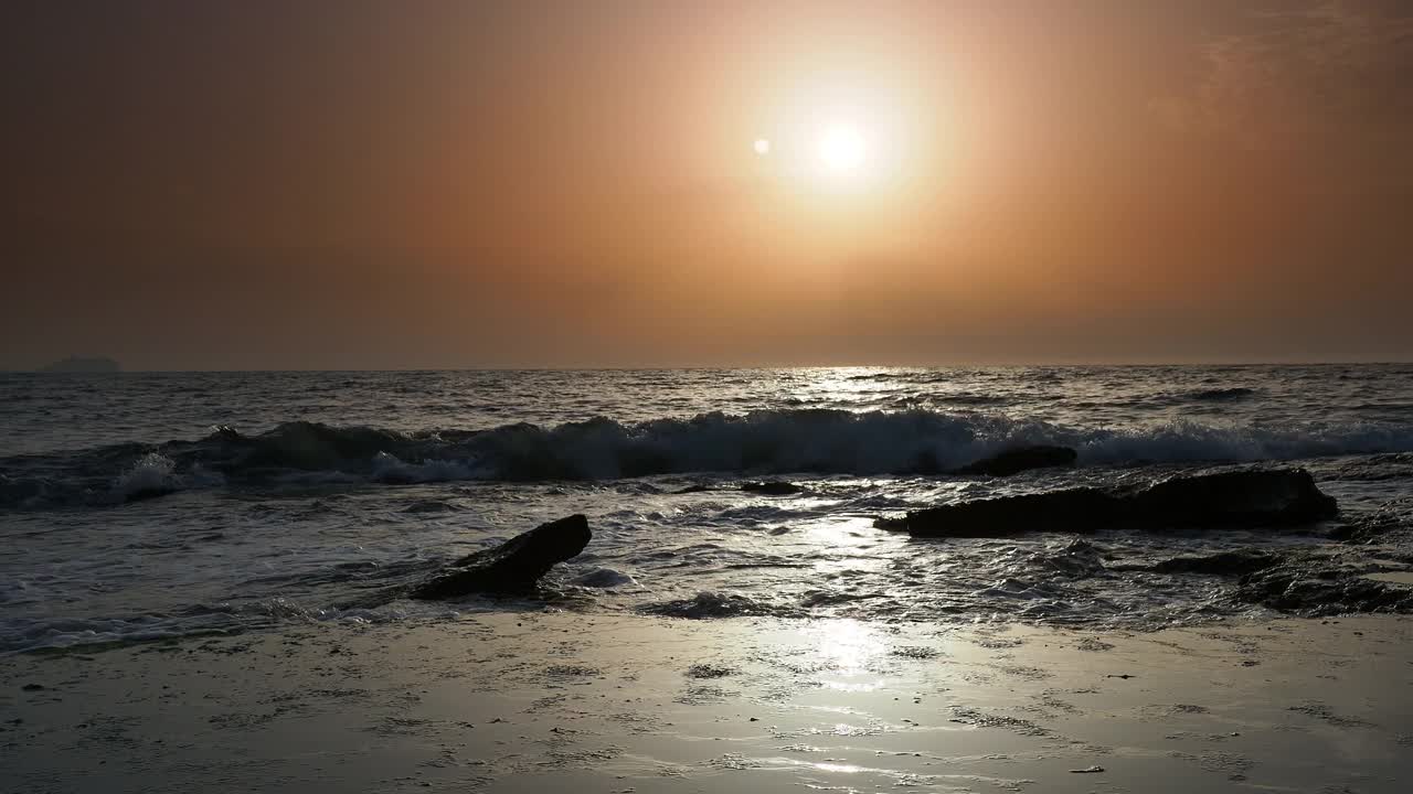 日出时的海岸线景观，太阳在地平线上，海浪拍打着海岸。视频素材