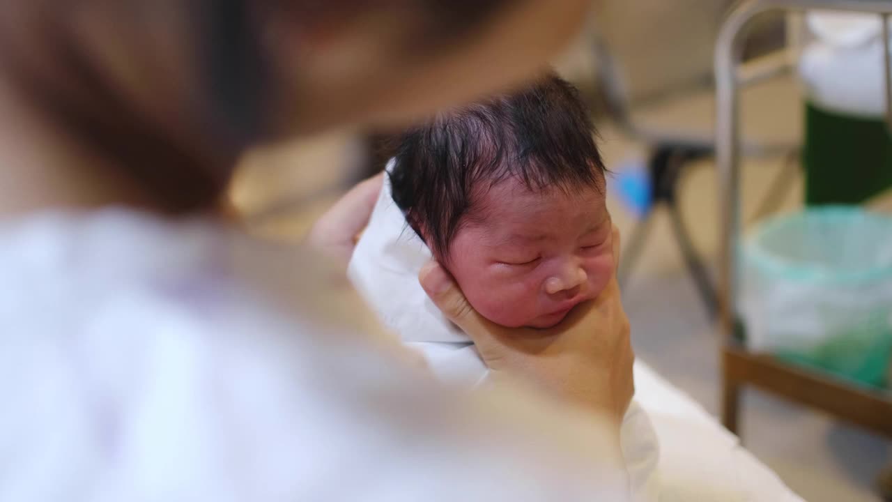 一名亚裔妇女在医院里抱着她刚出生的男婴。在这里，她斜倚着，抱着孩子靠近她的胸部安慰他。视频素材