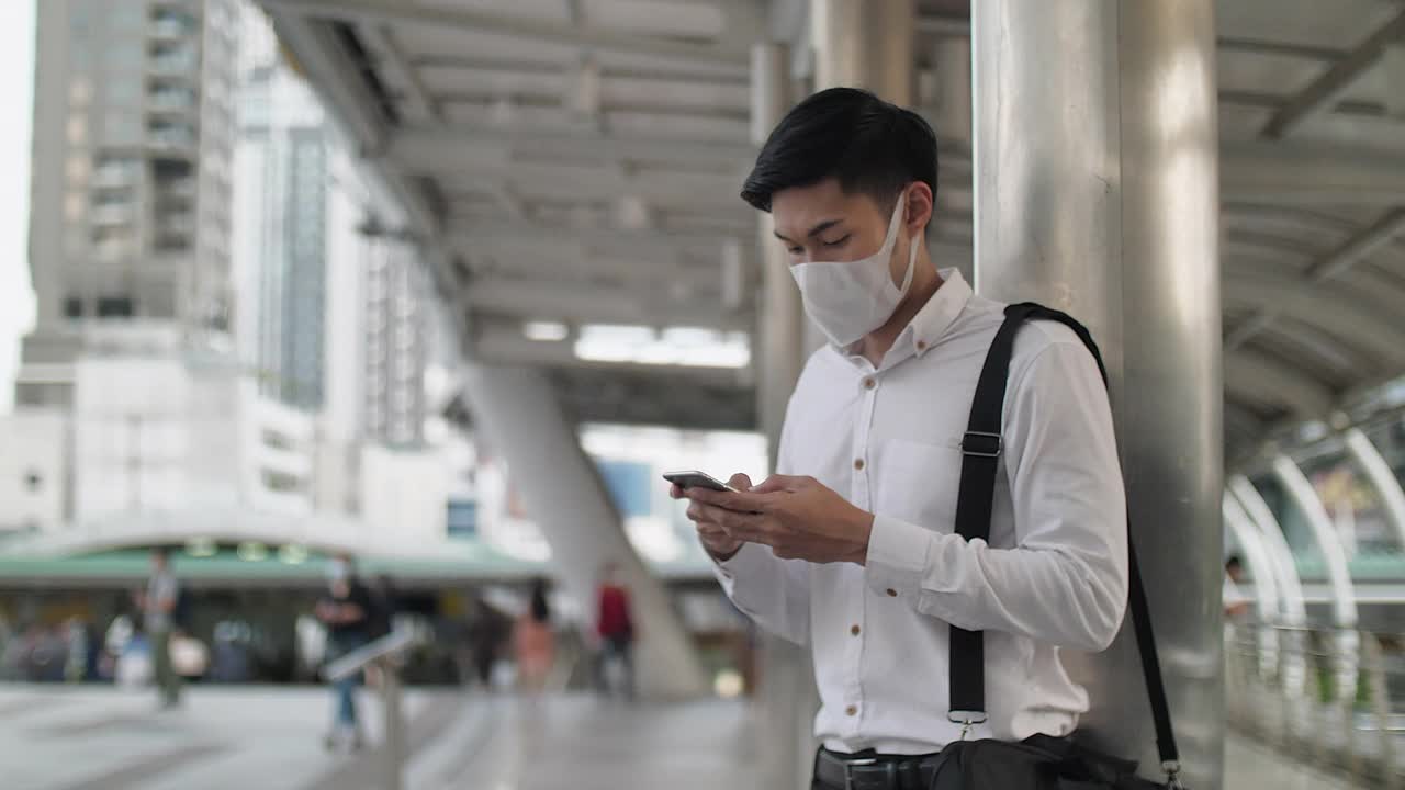 年轻的亚洲商人戴着口罩，使用智能手机视频素材