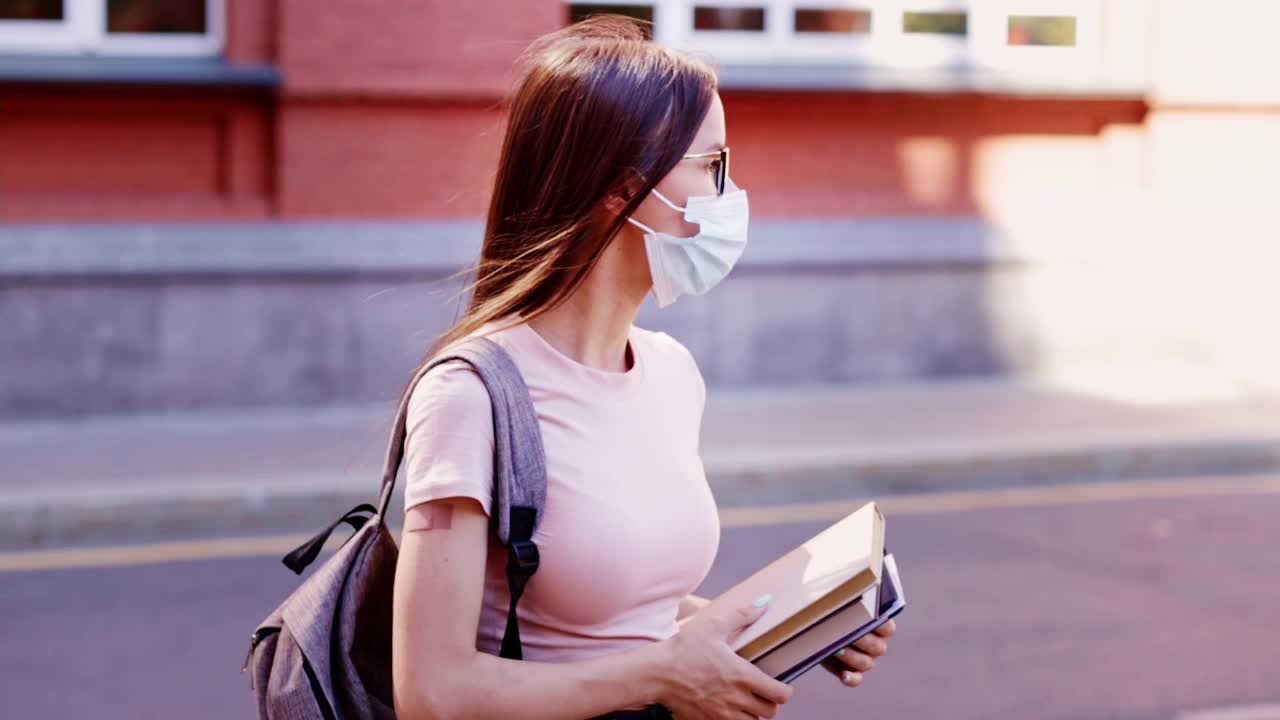 在学校和大学接种疫苗，十几岁的学生戴着口罩，手里拿着医用膏药站在大学旁边视频素材