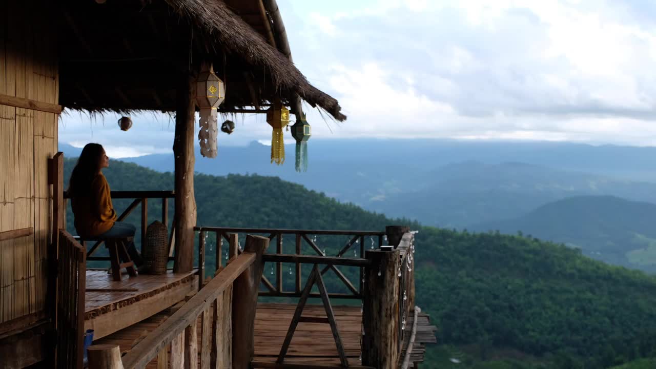 一个女旅行者坐在木屋里，看着美丽的山景视频素材