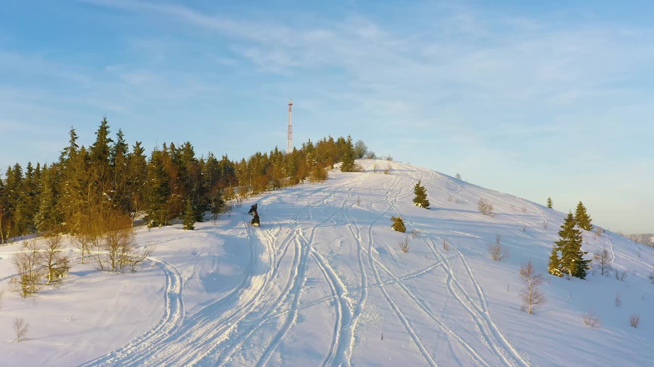 一名男子坐在雪地摩托上，沿着一条被雪覆盖的小路，在云杉树丛中快速驶向蜂巢塔视频素材