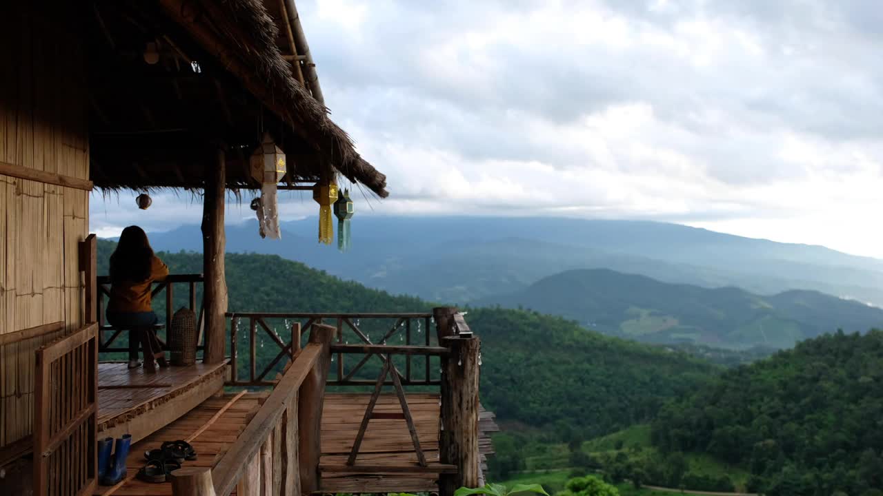 一个女旅行者坐在木屋里，看着美丽的山景视频素材