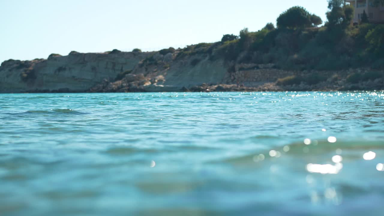 蓝色的地中海海浪在阳光中缓慢移动，背景是岩石海岸。阳光下湛蓝清澈的海水。塞浦路斯岛上美丽的自然风光。视频素材