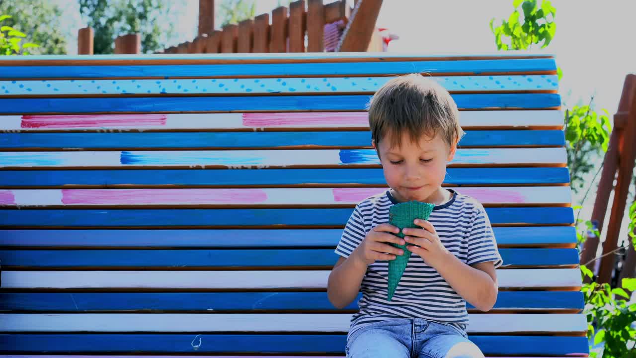 可爱的白人男孩坐在公园的长凳上吃冰淇淋视频素材