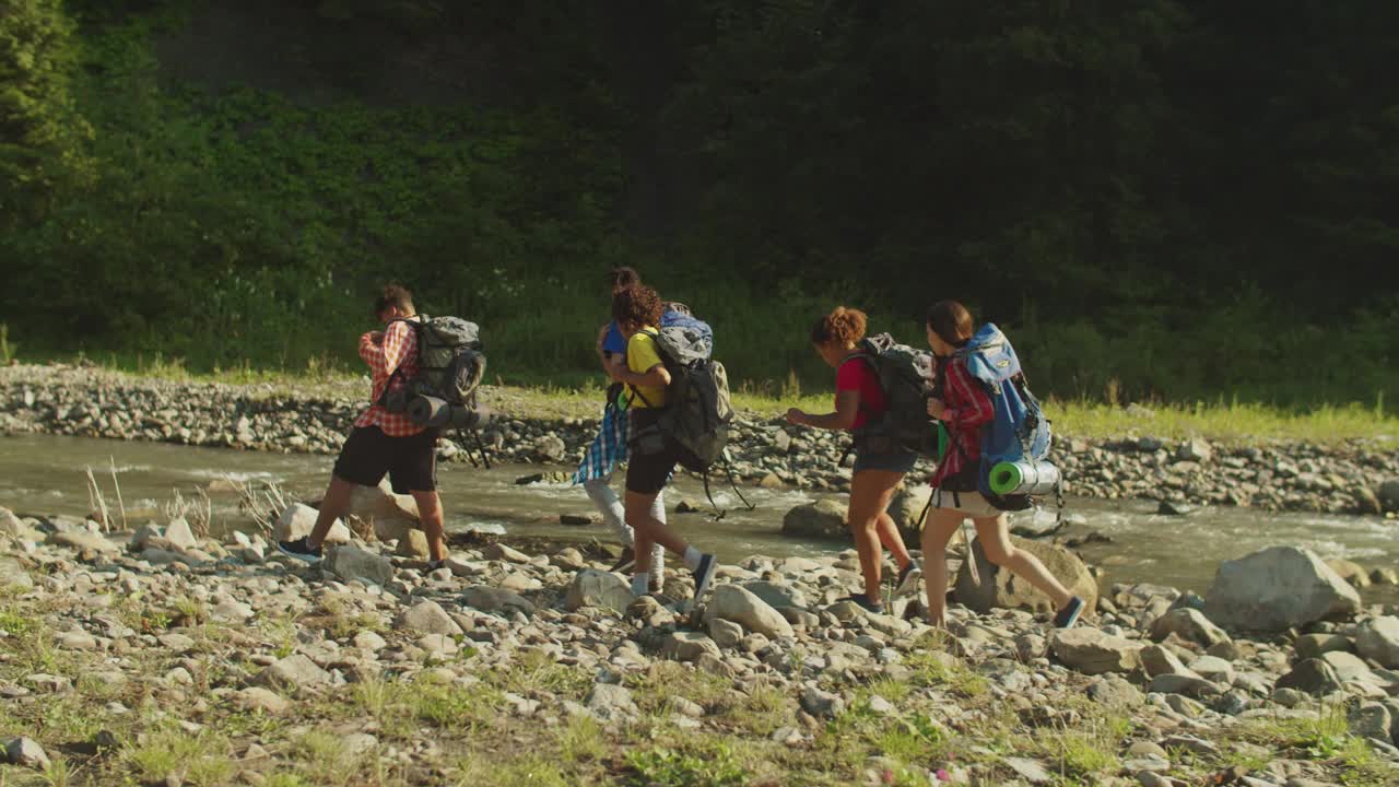 不同种族的徒步旅行者背着背包沿着山河徒步旅行视频素材